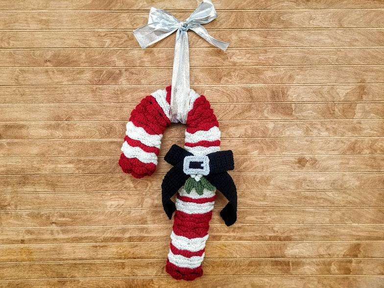 A red and white striped candy cane with a large black bow in the centre is hanging against a wooden wall.