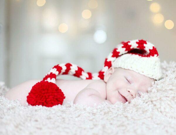 young baby lay on a fluffy blanket wearing a red and white striped crochet elf hat