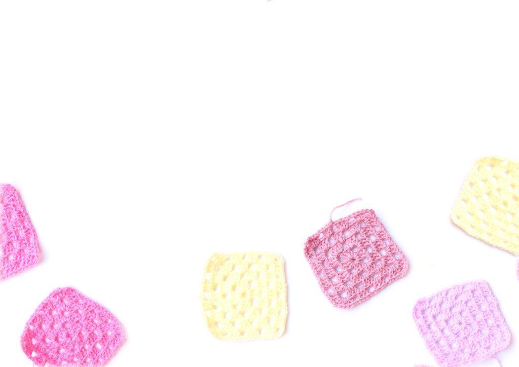 A collection of granny squares in shades of pink, purple and cream are displayed on a white background. 