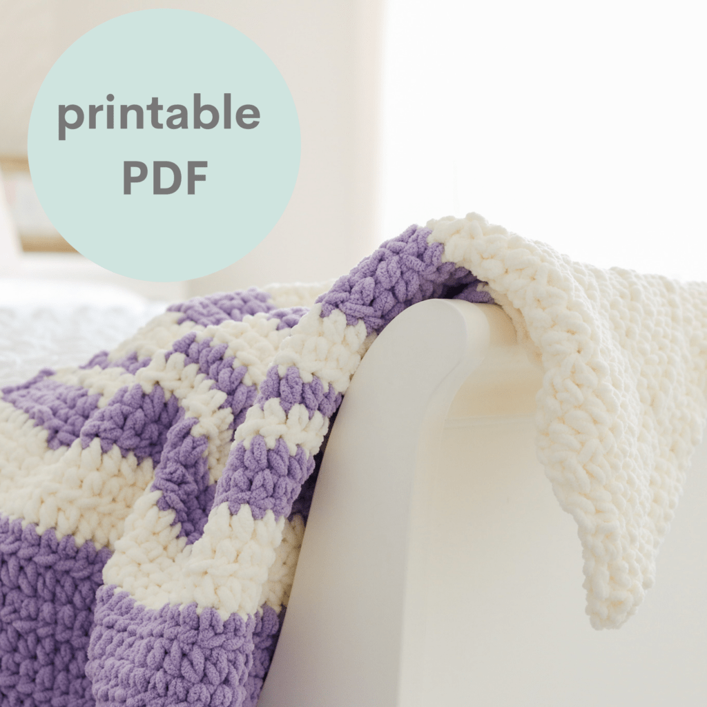 Stripy cuddly crochet baby blanket draped over a white bed