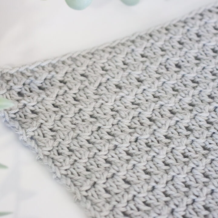 Floret stitch in grey yarn on a white background next to a plant.