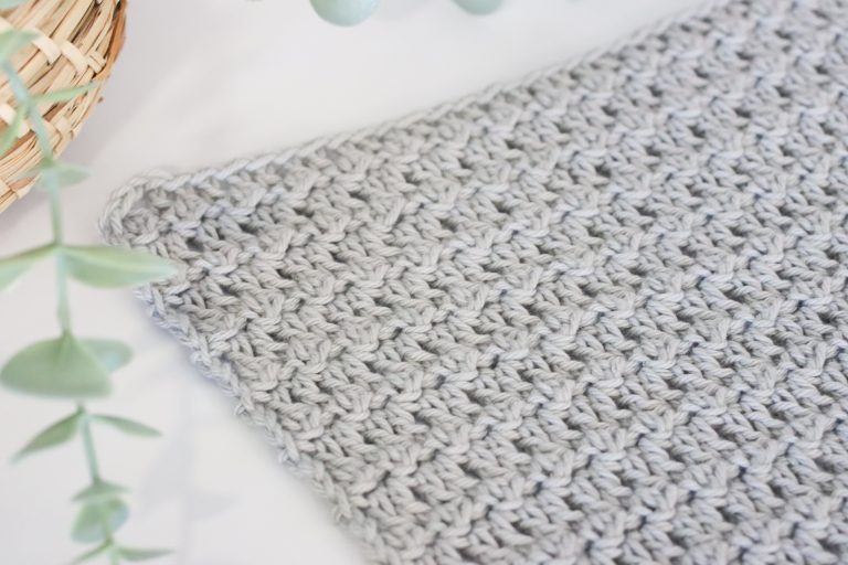 Floret stitch in grey yarn on a white background next to a plant.