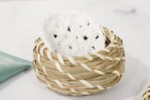 crochet face scrubbie made from white cotton yarn sat in a small wicker basket