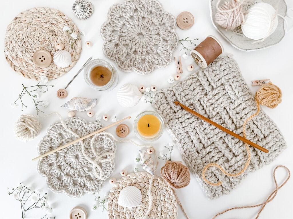 a flat lay image of neural, beige and cream objects including a coaster, swatch of the basket weave stitch, shells, wooden buttons, beads and wooden crochet hooks. 