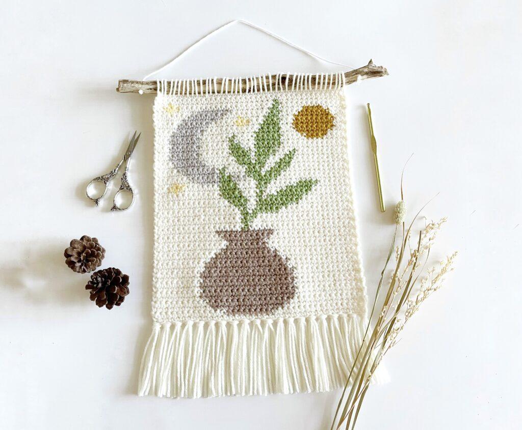 The Oh So Boho wall hanging is displayed on a white background besides a pair of pinecones, silver scissors and some dried grass.