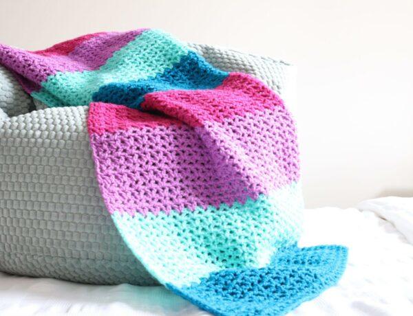 Jewels Blanket on a foot stool showing the drape in pink, purple, turquoise and blue yarn.