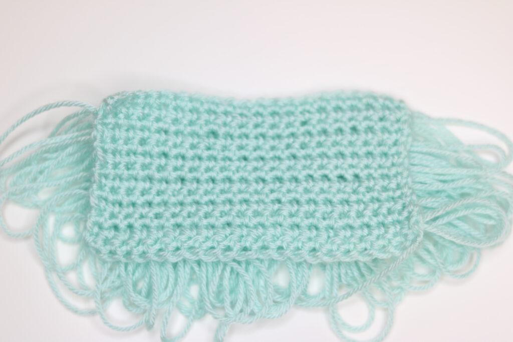 A swatch of loop crochet stitch in aqua yarn sits on a white background. The back is displayed.