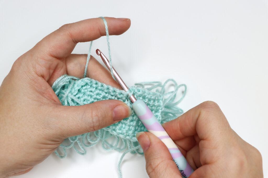 An in progress swatch of loop crochet stitch in aqua yarn.