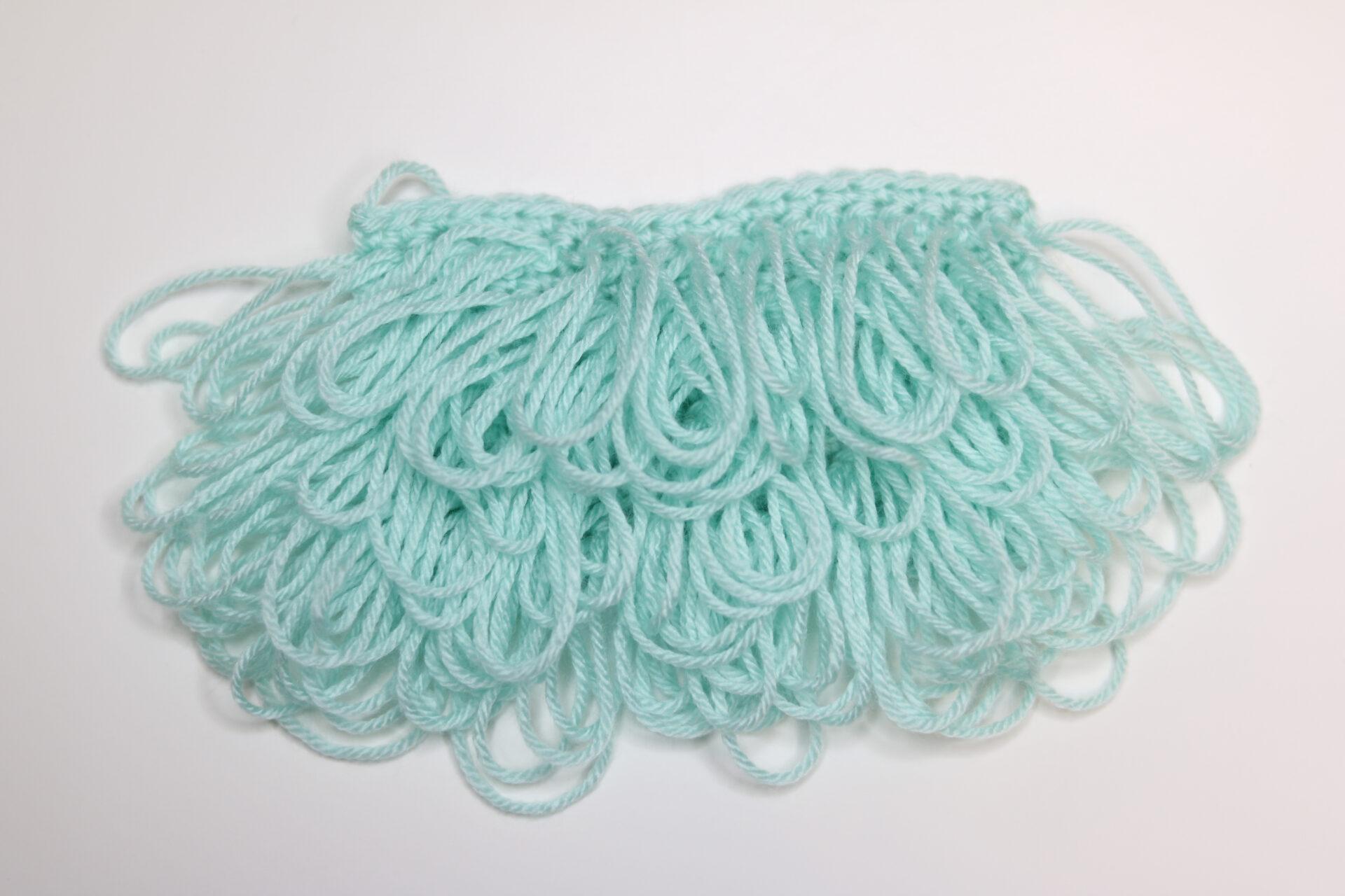 A swatch of loop crochet stitch in aqua yarn sits on a white background. The front is displayed.