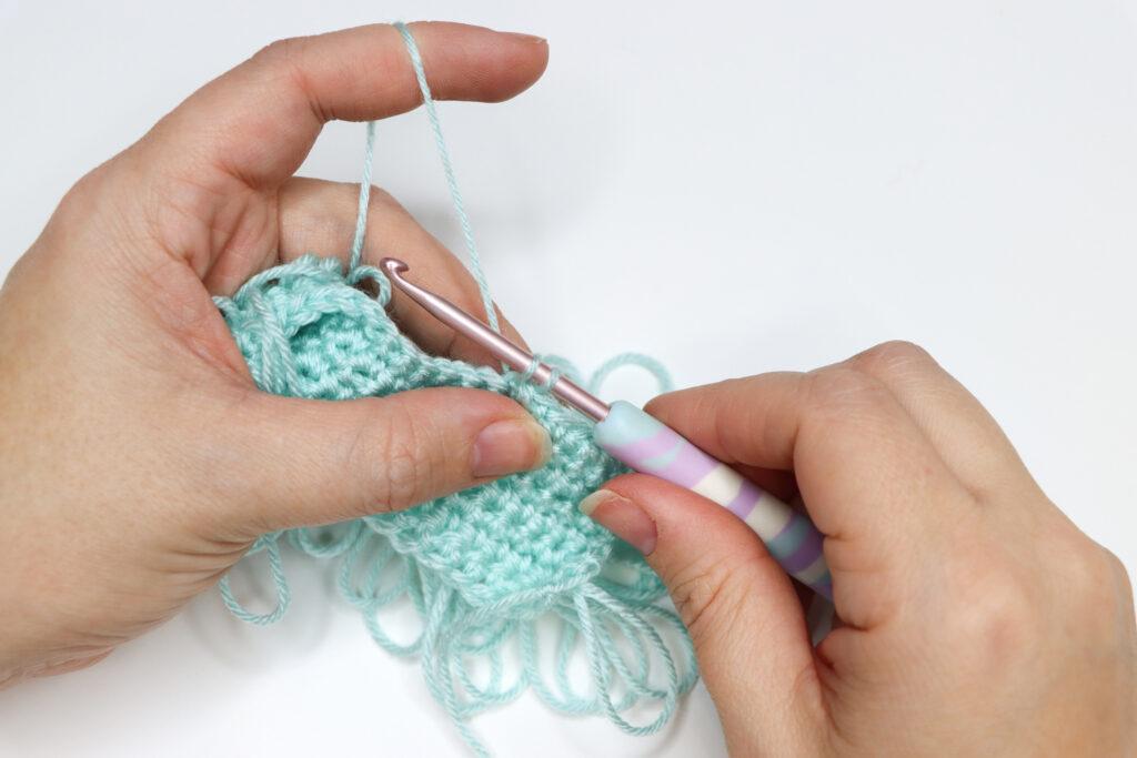 An in progress swatch of loop crochet stitch in aqua yarn.