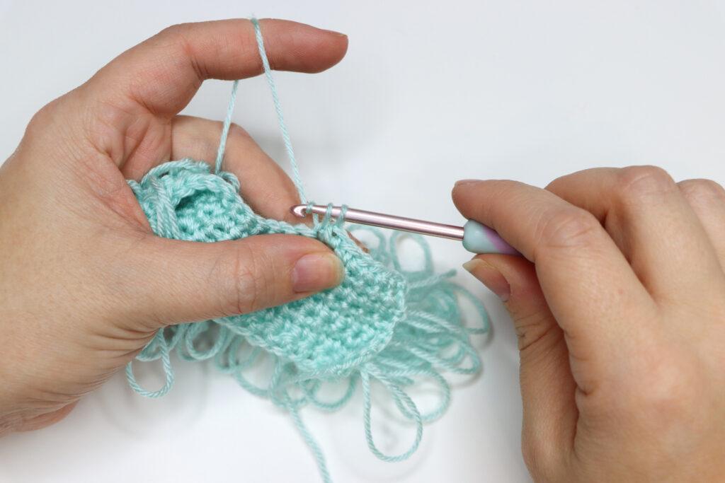 An in progress swatch of crocheted loop stitch in aqua yarn.
