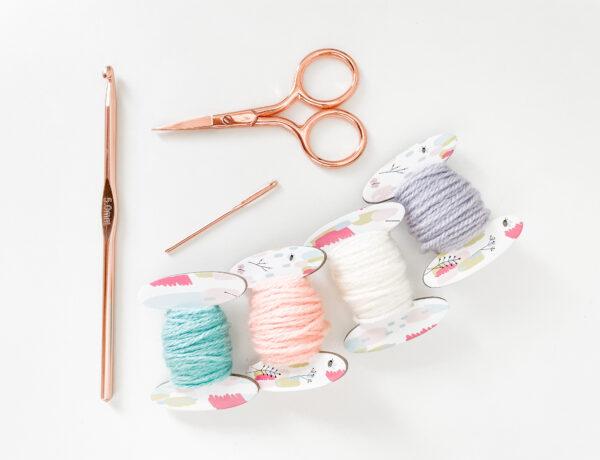 Yarn, scissors, crochet hook and needle as a flat lay on a white background.