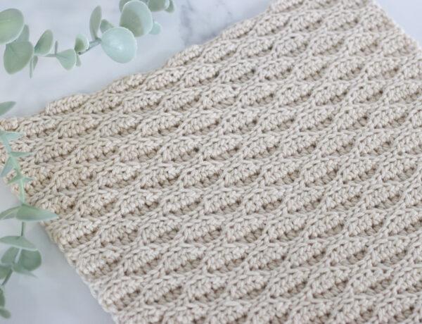 Almond Ridges crochet swatch on a marble background with a plant.