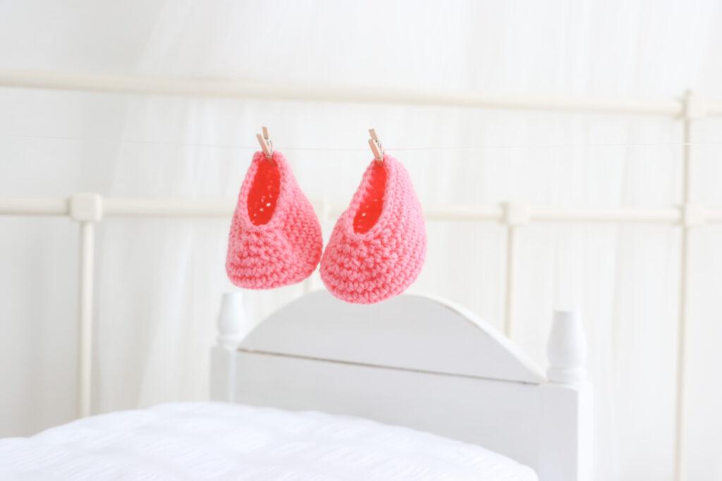 A pair of crochet baby booties in coral are pegged onto a white string.