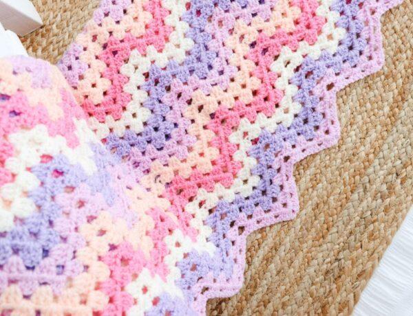 A granny ripple blanket with pink, fuchsia, white, purple and peach stripes.