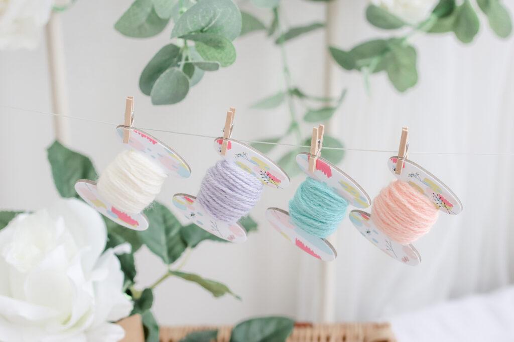 A string of bobbins with pastel colours yarn in cream, lilac, blue and peach is strung up.
