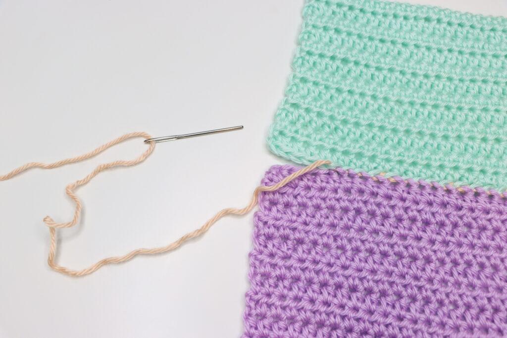 A pair of female hands is shown demonstrating how to to the mattress stitch. The swatch is purple, aqua and peach, bright colours so that the stitching is clearly demonstrated.