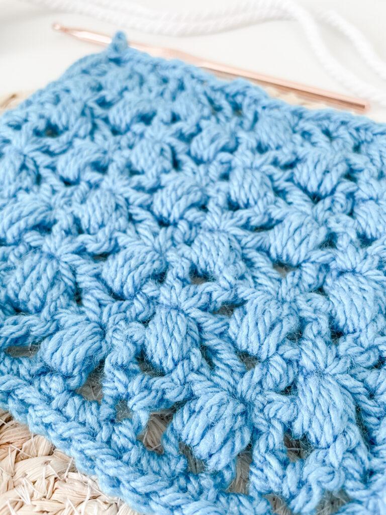 A close-up shot of the lace cluster stitch. The stitch is open, lacy and vintage-style and is made using a bright blue yarn.