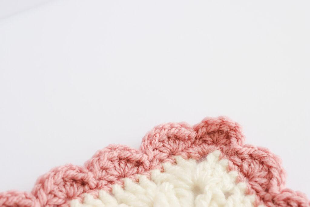A swatch of shell edge border is displayed. The swatch is made from white yarn with the border made from a dusty rose colour. 