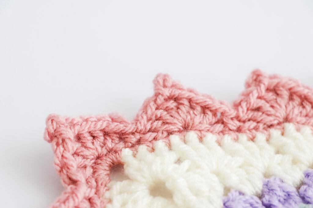 A swatch of triangle picot edge border is displayed. The swatch is made from white yarn with the border made from a dusty rose colour. 