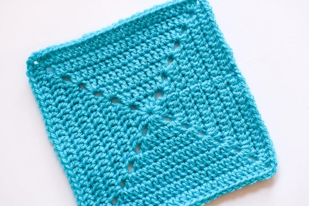 A solid granny square made from rich coloured blue yarn sits on a white background. 
