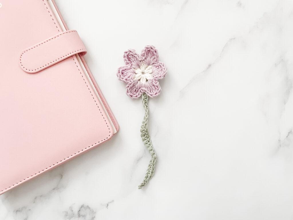 daisy crochet bookmark lay alongside a pink planner 