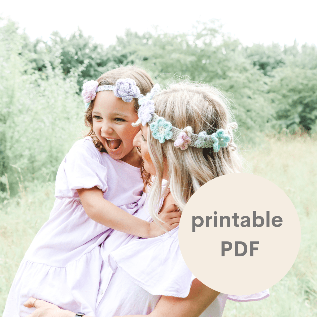 A mum and daughter in crochet flower crowns laughing in a field.