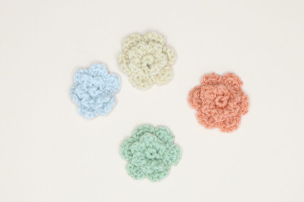 4 simple crochet flowers in light blue, Cream, Green and orange.