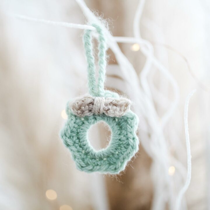 a mini crochet wreath made in pale green yarn with a cream bow hanging from white sparkly branches