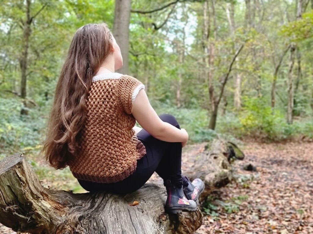 Brown crochet t shirt being modelled by a girl outside sat on a log.