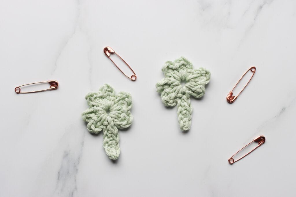 two crochet shamrock motif pictured with four safety pins to show how you can turn the shamrock into a brooch.