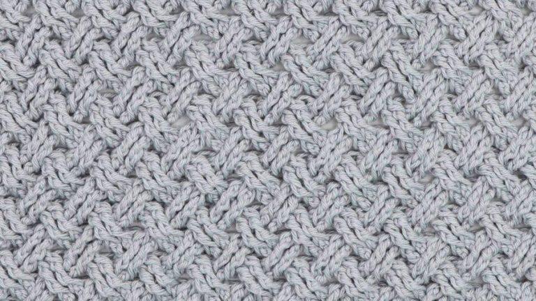 Close-up of a crochet fabric made with the Celtic Weave stitch in light grey yarn, showing an interlocking, textured pattern resembling braided cables.