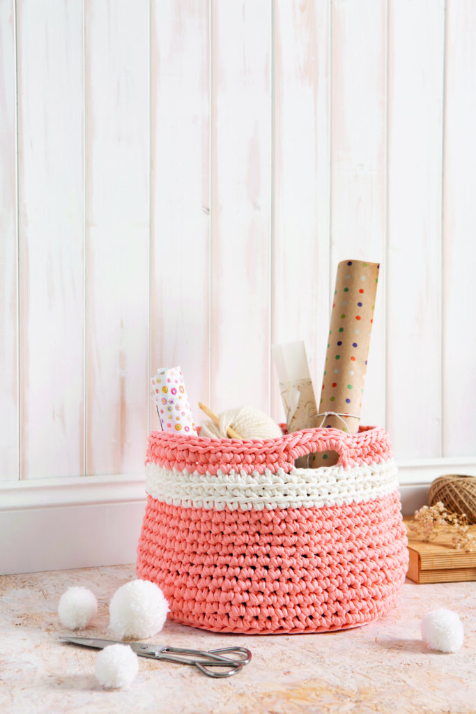 A yarn basket with handles filled with gift wrap and stationery.