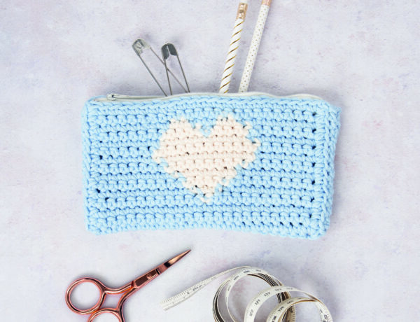 A blue pencil case featuring a white heart with stationery coming out of it photographed as a flat lay.