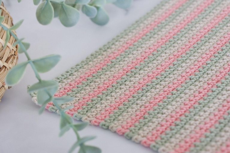 a swatch of UK double crochet using three colours of yarn in paintbox cotton dk in colours: pistachio, vanilla cream and blush pink. The swatch of double crochet is lay on a marble background with a green trailing palm tin the top left corner of the image.