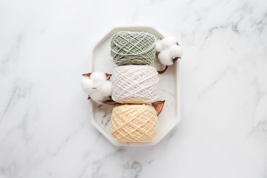 Image of 3 yarn cakes in pistachio, white and yellow, placed on a marble tray with a marble background.