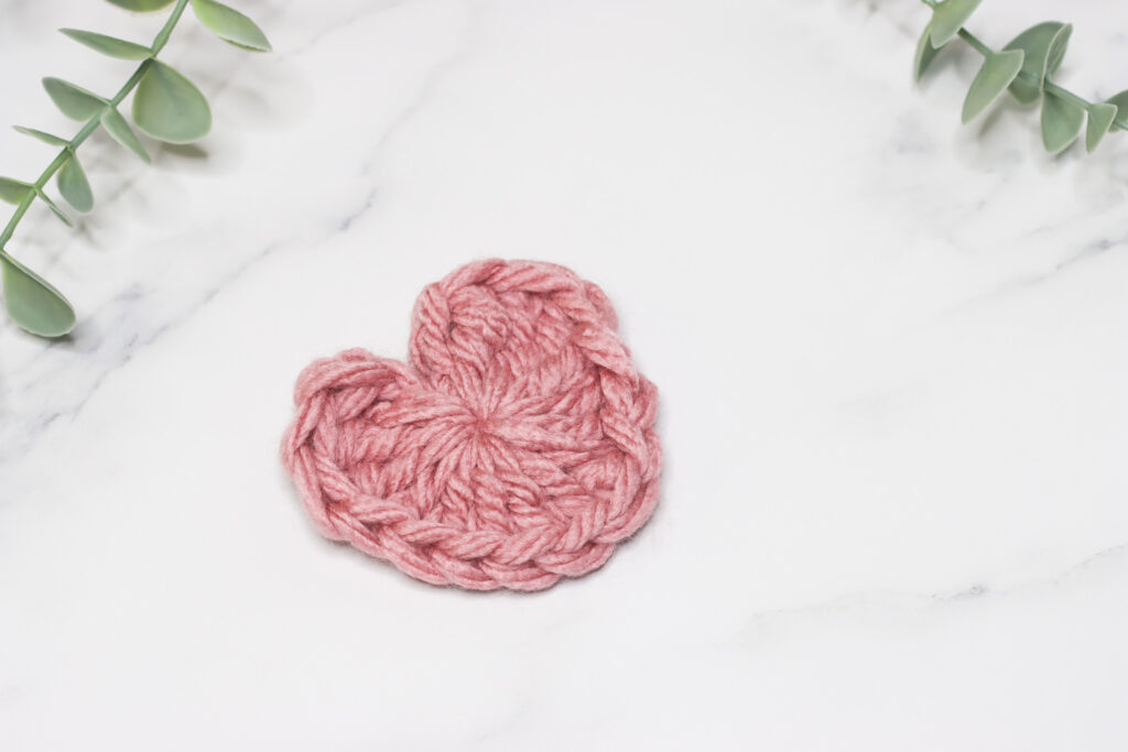 Crochet heart made in dusky pink yarn laid on a marble background with a hint of green foliage