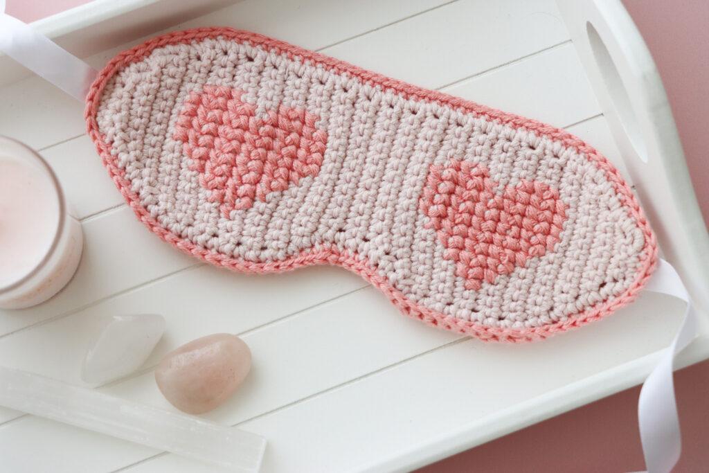 crochet sleep mask ob white tray alongside a pink candle and three crystals