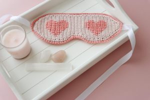 crochet sleep mask ob white tray alongside a pink candle and three crystals