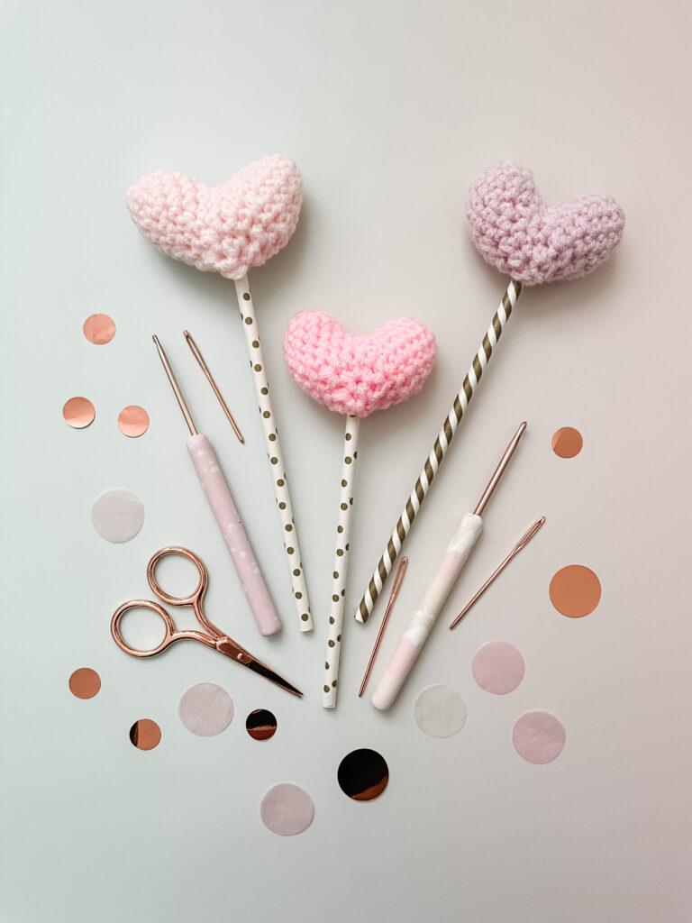 Crochet hearts on the top of straws surrounded by confetti and scissors.