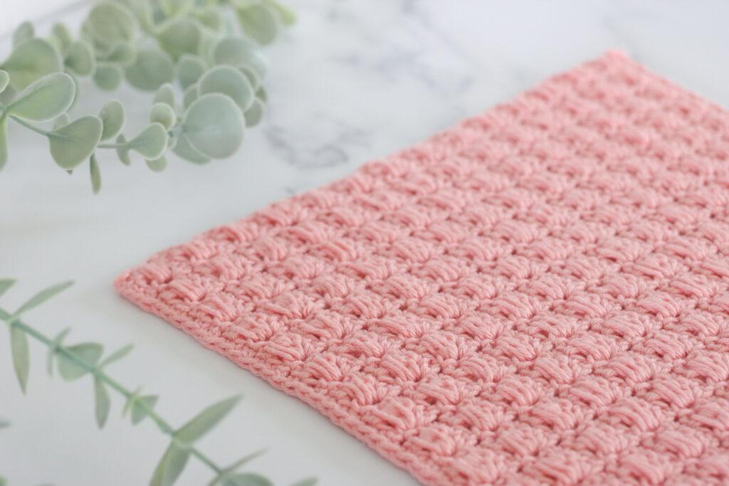 Pink blocked bead stitch crochet Swatch on a marbled background with a plant.