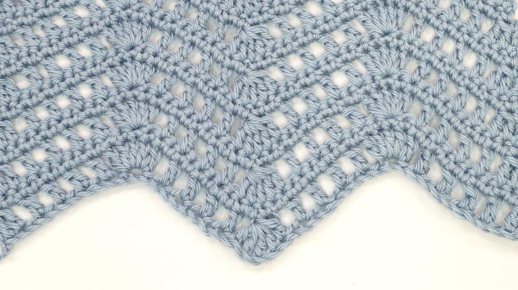 The lacey ripple stitch in blue yarn on a white background.