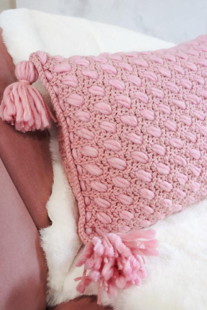 a pink textured cushion sat on a pink chair with a cream faux fur rug draped over it.
