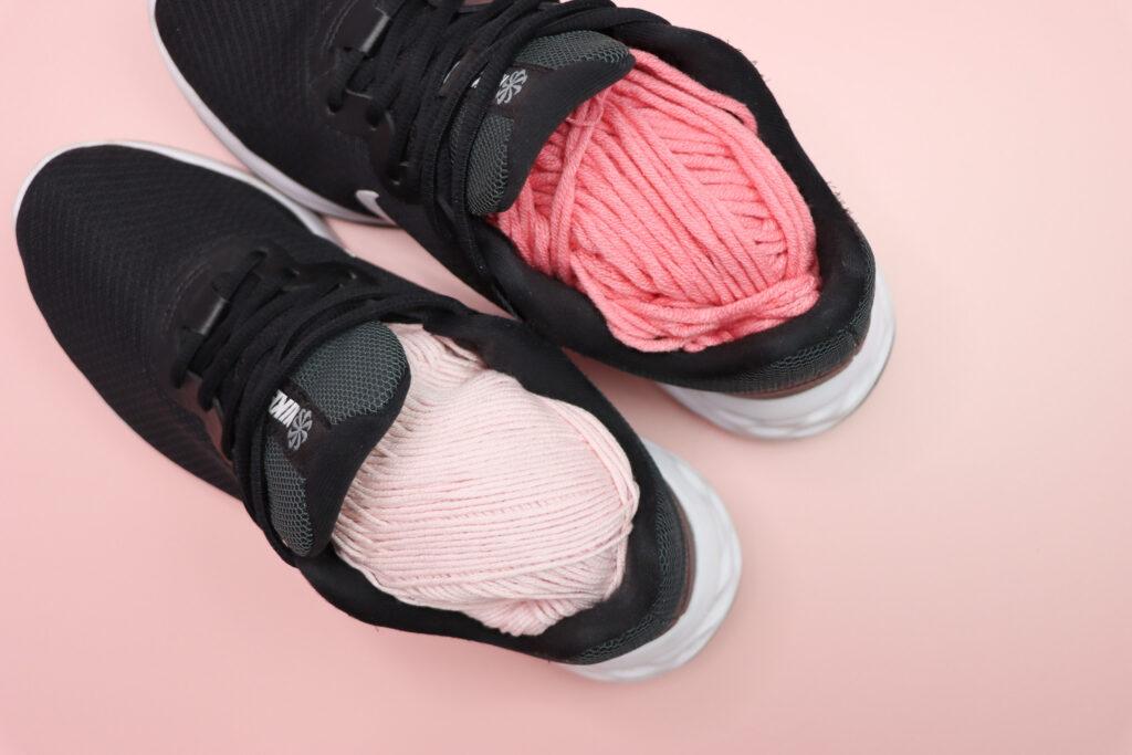 two skeins of yarn inside a pair of black trainers lay flay on a pink background to illustrate a packing hack for when you take your yarn on holiday with you. 