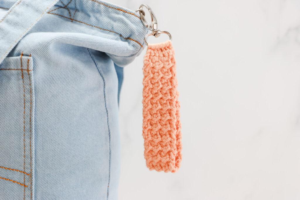 Keychain on a denim bag made from orange crochet on silver hardware.