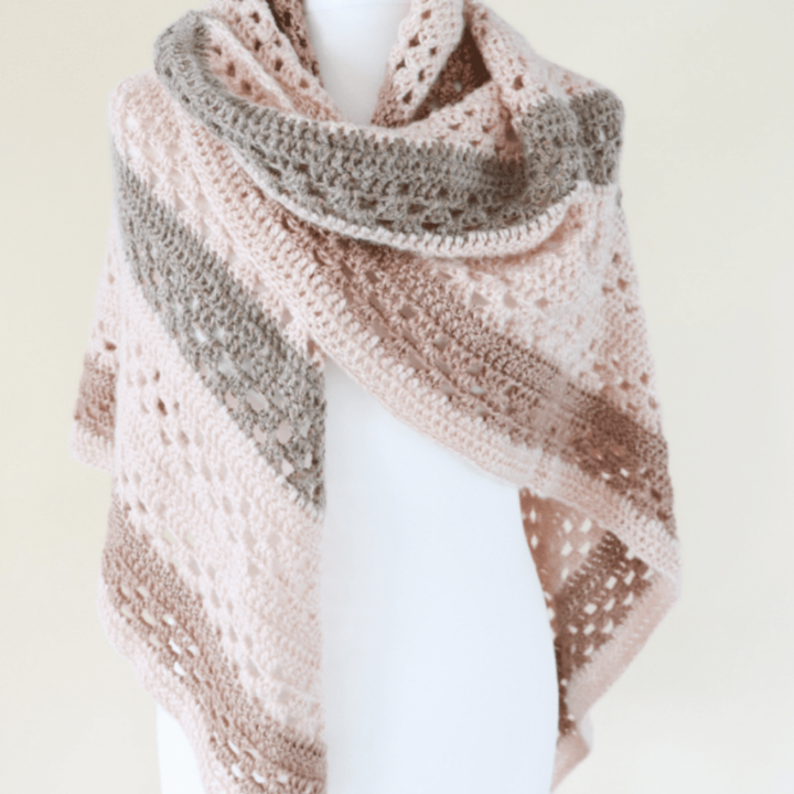 Crochet shawl on a white mannequin in peach, grey and brown yarn.