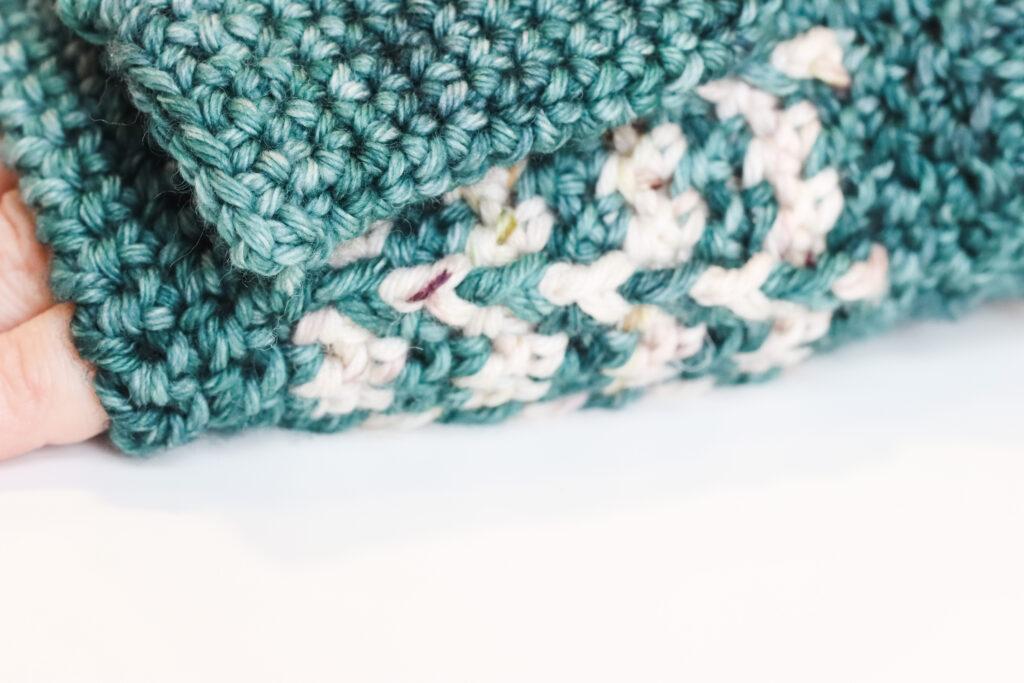 one hand lay flat on a white table wearing a crochet wrist warmer. The image is a close-up on the textured stitch. 