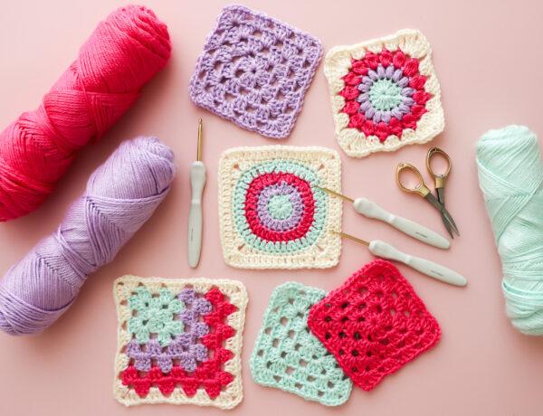 crochet granny squares, yarn and equipment lay flat on a pink background
