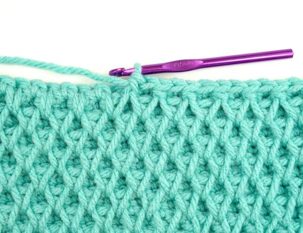 a swatch of honeycomb stitch with aqua yarn and a purple hook