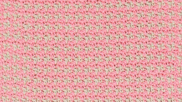 Close-up of a pink and cream crochet swatch demonstrating the houndstooth stitch pattern, showing a repeating, textured design made with alternating colours.